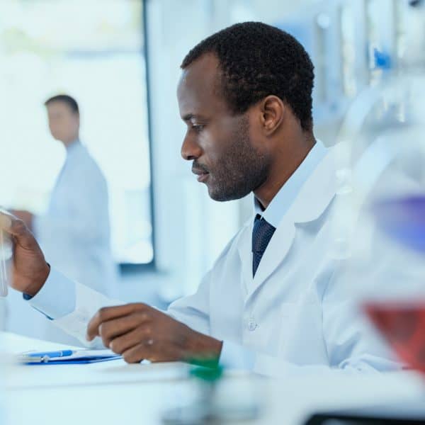 Side view of african american scientist in white coat holding and examining test tube with reagent laboratory researcher concept
